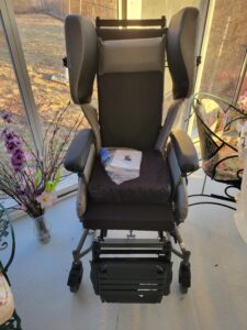 manual wheelchair with cushioned seat, arm rests, foot rest, and a head rest with additional cushions on the side