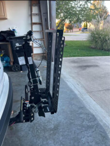 wheelchair lift attached to the back of a vehicle with the ramp folded up. Device contains wires implying that it is electric