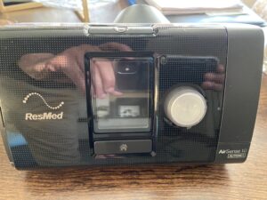 Front of CPAP machine. Machine is black with ResMed logo. There is text on the machine that says “AirSense 10 Autoset.” Like new condition, but slightly dusty.