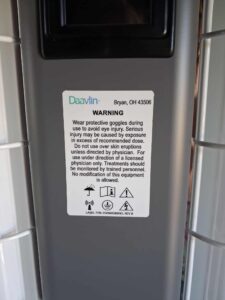 Warning sticker on lamp frame. Text says, “Warning. Wear protective goggles during use to avoid eye injury. Serious injury may be caused by exposure in excess of recommended dose. Do not use over skin eruptions unless directed by physician. For use under direction of a licensed physician only. Treatments should be monitored by trained personnel. No modification of this equipment is allowed.”