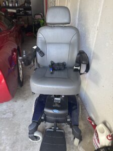 Gray cushioned electric wheelchair with seatbelt. Chair has a smooth texture that may be leather. Gently used.