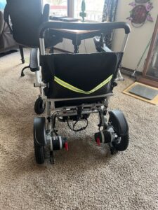 Back of electric wheelchair. A storage pocket with a bright strap is attached to the back.