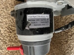 Close-up of slightly torn tag on electric wheelchair. Tag lists the rated voltage as 24VDC, the output power as 300W, and the rated current as 13.4A. There is also other information on the tag, but it is a bit harder to read due to the angle of the picture.