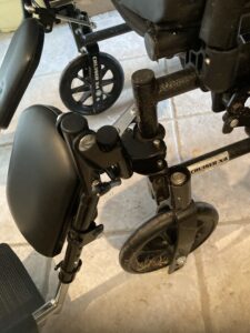 close up view of the smaller wheels on the front of the wheelchair, the padded leg rests and foot rests. Wheelchair says 