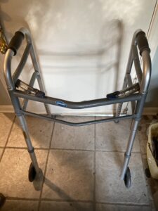 gray walker with u-shaped metal bars on each side, a padded handle on each bar, a bar in the front connecting them, 2 wheels on the front, and notches to adjust the height