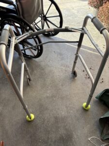 gray walker with u-shaped metal bars on each side, a padded handle on each bar, a bar in the front connecting them, 2 wheels on the front, 2 tennis balls on the back, and notches to adjust the height