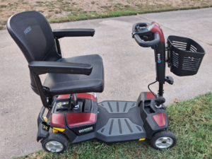 Side view of dark gray mobility scooter with red trim. Scooter has a basket attached to its front. The words “Go-Go Endurance Maxx Li” are visible on the side. Like new condition.