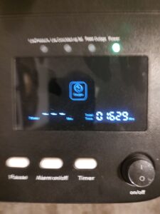 Close up of concentrator’s digital screen and the buttons next to it. Includes power button, timer, pause button, and alarm button. Picture is blurry.