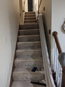 set of stairs with a white rail for the stair lift on one side. There is a large platform about two thirds of the way up the stairs, and the stair lift rail follows that pattern