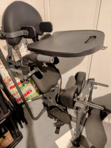 black vertical device with head rest, tray, a foot platform, and cushioned areas in the middle to support the body