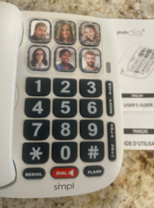 Blurry close up of white photo phone. Has large black buttons with white numbers. Above the numbers are six more large buttons. You can insert a picture into each of these six buttons. Like new condition.