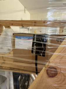 Close up of small box inside crate. Box has a sticker that lists the items that are included in the unit, but most of the text is illegible due to the image quality.