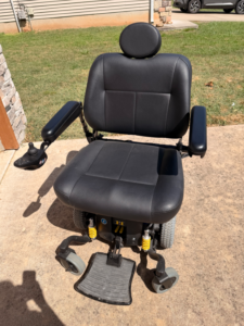 Front view of black power chair. Joystick, headrest, armrests, footrest, and seat and back cushions are visible. Like new condition.