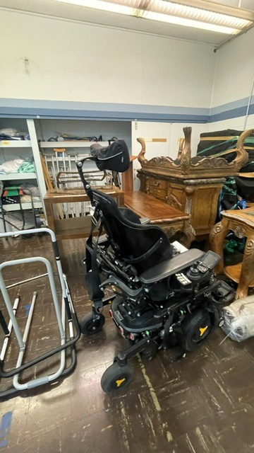 Back view of black power chair. Joystick, armrests, and headrest are visible. Fair condition.