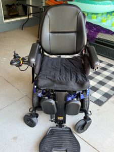 Front view of black power chair with blue base. Back cushion has a smooth texture that may be leather. Seat cushion has a wrinkled seat cover. Seat cover is a different shade of black and has different fabric textures compared to the back cushion. Other than that, chair is in gently used condition.