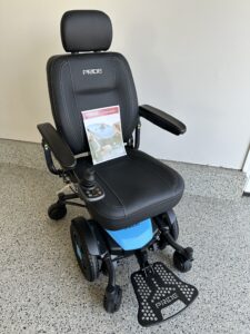 Black power chair with an owner’s manual propped up on the seat. Chair has a smooth texture that may be leather. The base of the chair is a medium blue. Like new condition.