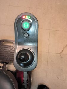 Close up of control panel, located by armrest. Includes joystick, button with horn symbol on it, and glowing power button. Surface is scratched.