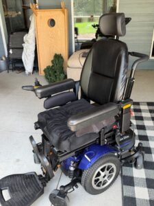 Three-quarter view of power chair, facing left. Attendant handle is visible.