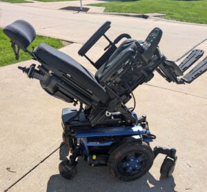 Side view of black power chair with blue base. Chair has been titled far back on its base for this picture.