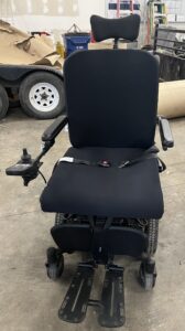 Front view of black padded power wheelchair with seatbelt and footrests. Gently used condition.