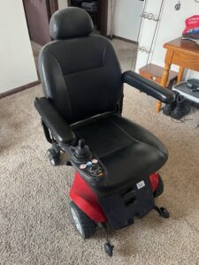 Black power wheelchair with red base. Chair has a smooth texture that may be leather. Gently used condition.