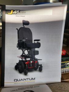 Owner’s Manual for J4E. The manual displays a picture of the power chair, which is black, padded, and has a red base.