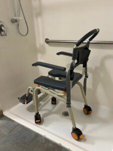 side/back view of shower chair showing handle bar to push and wheels on the bottom