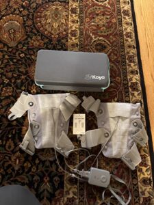 Gray Koya case and 2 compression sleeves with straps and buckles, an attached control unit with cables